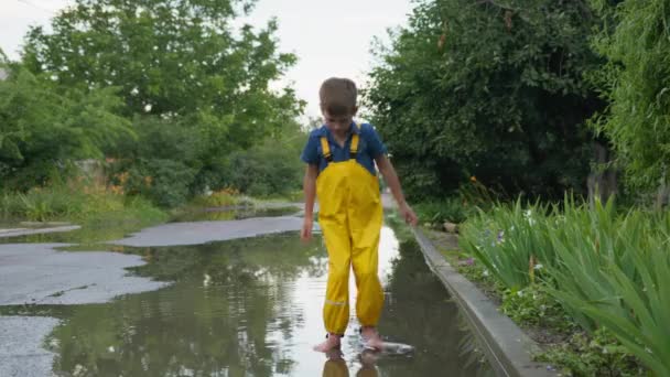 Liburan musim panas, bertelanjang kaki gembira anak laki-laki menikmati permainan di genangan melompat-lompat dan tertawa oleh jalan — Stok Video