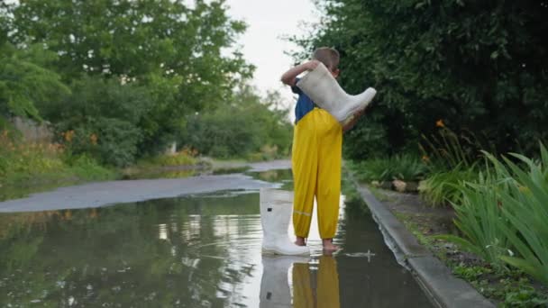 Estilo de vida, lindo niño varón en overoles disfruta jugando en charco y vierte agua de la bota de goma en el día cálido después de la lluvia, la temporada de verano — Vídeos de Stock