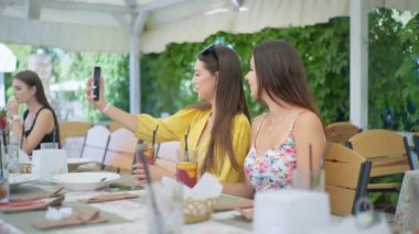 Çevrimiçi iletişim, restoranda çekici genç kızlar ve kafede otururken akıllı telefondan arkadaşlarıyla sohbet etmek.