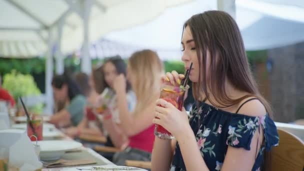 Lifestyle, krásná mladá dívka pije lahodný chladný koktejl při relaxaci v kavárně nebo restauraci a komunikuje se svými přáteli sedí u stolu — Stock video