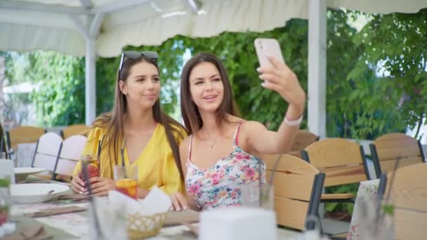 Mujeres jóvenes almorzan en el restaurante y hablan con amigos en línea a través de videollamadas en teléfonos inteligentes — Vídeos de Stock