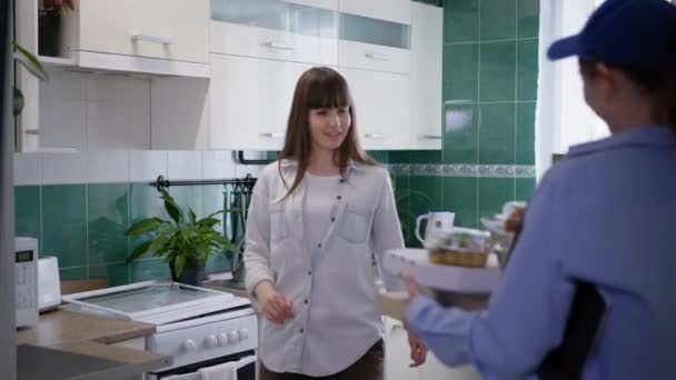 Thuisbezorging, vrouwelijke klant krijgt online bestelling met voedsel door meisje koerier op keuken — Stockvideo