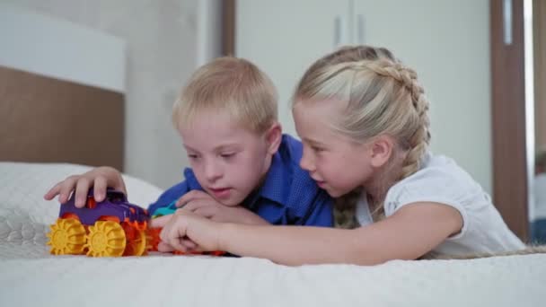 Spielen mit Autos, fröhliche Schwester und kleiner Junge mit Down-Syndrom haben Spaß mit Spielzeug auf dem Bett, dann kitzelt Mädchen ihren Bruder zu Hause — Stockvideo