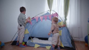 İki çocuk yatak odasında kalıyor, küçük kardeşler çadırı bayraklar ve çelenklerle süslüyor.