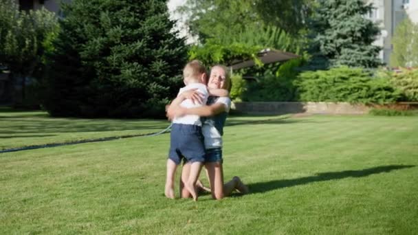 Vacanza allegra, ragazza positiva senza denti cattura e abbraccia il suo fratellino mentre cammina nel parco sul prato verde — Video Stock