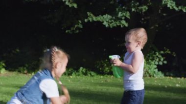 yaz parkı açık havada, çocuk su serpti ablasının üzerine yeşil ağaçların arka planına