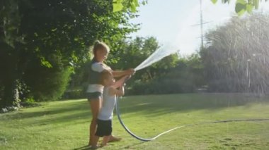 Aile yaz tatili boyunca kır evinin arka bahçesinde, çocuklar su ve hortumla oynuyor.
