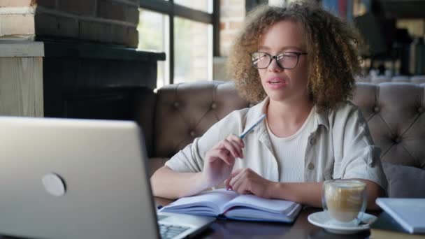 Avlägsen utbildning, ung flicka talar om video kommunikation på laptop när du sitter vid bordet i caféet — Stockvideo