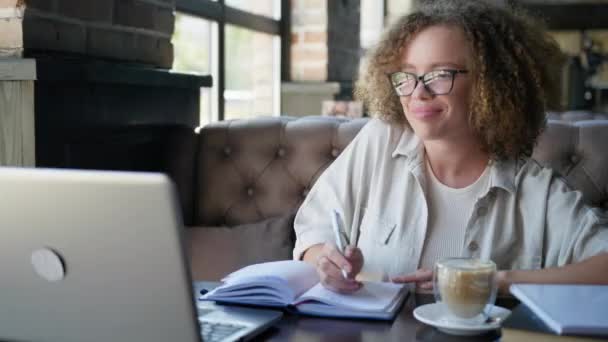 Kształcenie na odległość, młoda kobieta rozmawia z nauczycielem przez łącze wideo na laptopie siedzi przy stole w kawiarni — Wideo stockowe