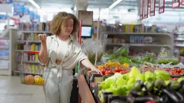 Retail, woman with basket in hands buys fresh vegetables and fruits in grocery store — Stock Video