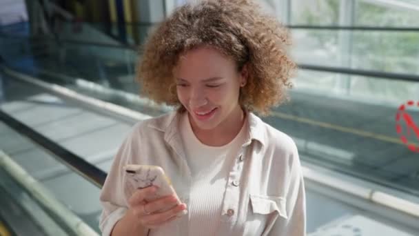 Жінка зі смартфоном в руках рухає ескалатор в торговому центрі — стокове відео