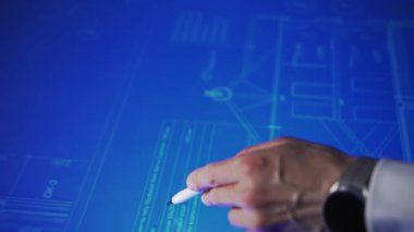 In an office, leaning over a large monitor instead of a desk, a man actively uses an interactive diagram on the screen. The camera focuses on his hand with a stylus, actively interacting with an