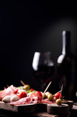 Çeşitli et ve kiraz mozzarella peyniri, bir şişe şarap ve arka plan üzerinde cam ile ahşap kesme tahtası. İtalyan antipasti