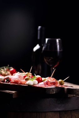 Çeşitli et ve kiraz mozzarella peyniri, bir şişe şarap ve arka plan üzerinde cam ile ahşap kesme tahtası. İtalyan antipasti
