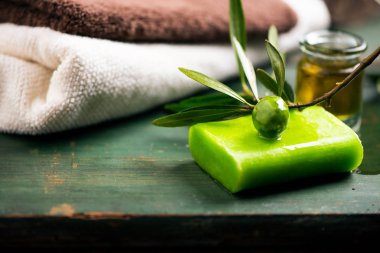 Natural spa with olive oil bar soap and towels onn a green wood vinatge table clipart