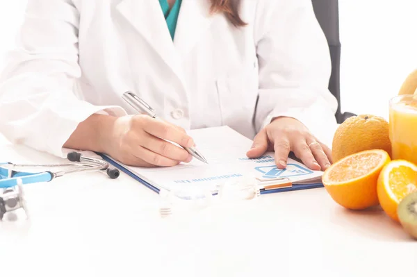 Nutritionist writing medical records and prescriptions with fresh fruits