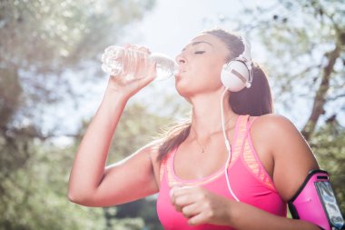 Tatlı su içme ve müzik kulaklık eğitimden sonra susamış kadın koşucu. Park açık havada egzersiz genç atletik kadın. 
