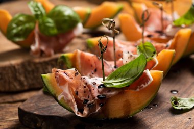 Jambon ve fesleğen yaprakları ile dilimlenmiş kavun, bir odun doğrama servis