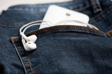 Mavi kot pantolon ve beyaz kulaklık ön cebinde Smartphone
