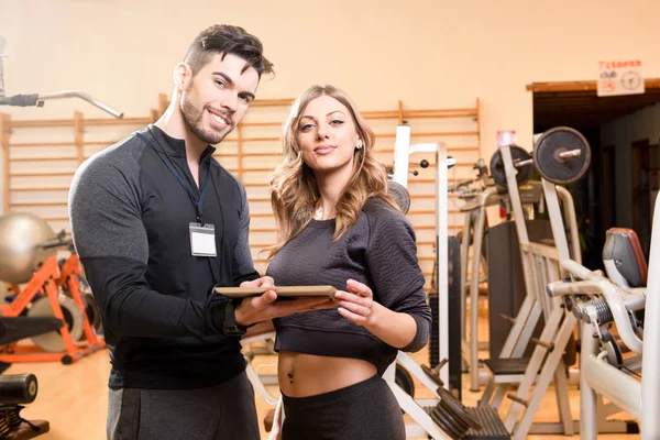 Sporty man ad woman using pc tablet at gym. Couple of young fitn