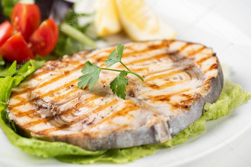 Grilled wordfish with salad and lemon on the white plate 