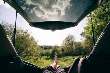 Adam arabanın bagajında oturmuş ormana bakıyor. Güzel manzara manzarası. Yolculuk konsepti