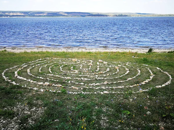 labyrinth lined with stones on river bank.