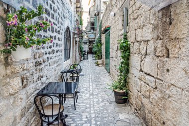 Dar sokak içinde tarihi kent Trogir, Hırvatistan. Sabah sahne. Seyahat hedef. Çiçekler, sandalye ve masa.