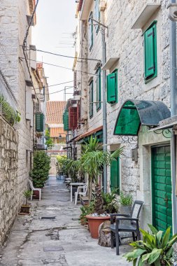 Dar sokak içinde tarihi kent Trogir, Hırvatistan. Sabah sahne. Seyahat hedef. sandalye ve bitkiler.