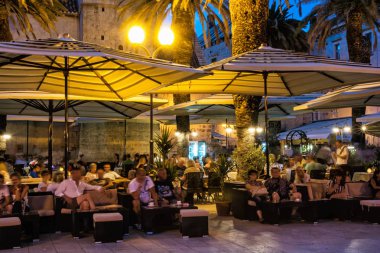 TROGIR, CROATIA - JULY 25, 2017: Many tourists are relaxing in an open-air bar at night, Trogir, Unesco, Croatia. Travel destination. Summer vacation. Illustrative editorial. clipart