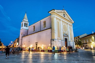 POREC, CROATIA - AUGUST 10, 2018: Lady of Angels Church, tourists and markets with souvenirs in Freedom square in Porec, Croatia. Evening time in summer vacation destination. Illustrative editorial. clipart