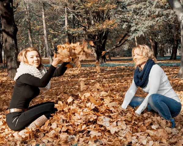 Två unga kaukasiska kvinnor kasta gula blad — Stockfoto