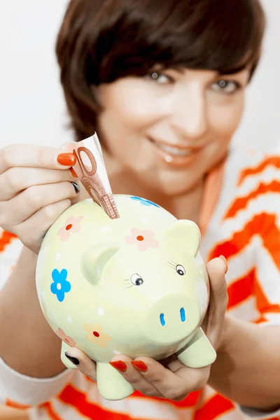 Woman gives money to piggy bank — Stock Photo, Image