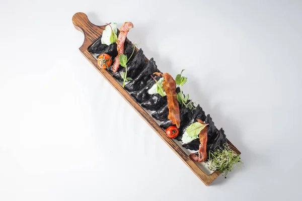 Ahşap tahta üzerinde siyah köfte zekâ pastırma, yeşil ve kiraz domates.