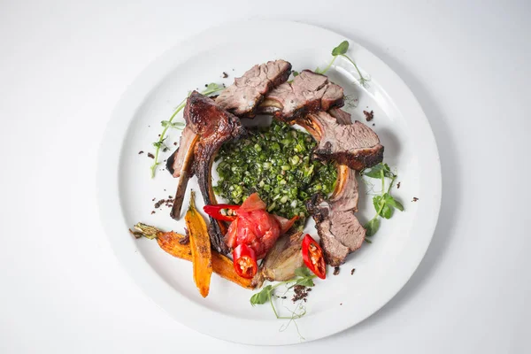 Baked lamb with carrot, onion, chili, green, carrot, green and tomatoes on white plate