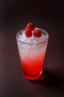Buz ve ahududu zarif koyu kahverengi zemin üzerine kırmızı kokteyl bardak.