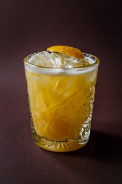 Sarı alkol buz ve zarif koyu kahverengi zemin üzerine limon dilimi ile kokteyl bardak.