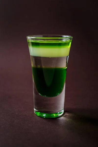 Green alcoholic shot glass with absent, irish cream, liquor on elegant dark brown background.