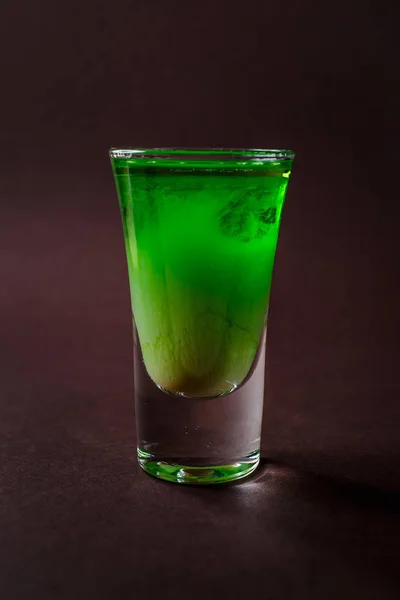 Green alcoholic shot glass with absent, irish cream, liquor on elegant dark brown background.