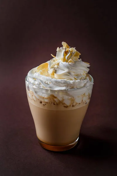 Glass of coffee with whipped cream and almonds shaving on elegant dark brown background.