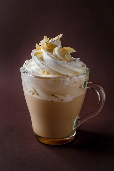 Glass of coffee with whipped cream and almonds shaving on elegant dark brown background.