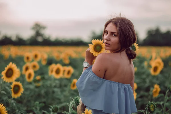 梦到穿着蓝色衣服的年轻女子抱着 夏天在向日葵的田野里嗅到向日葵 从她的背上看 回过头来看复制空间 — 图库照片