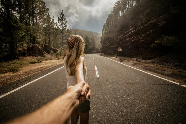 Jeune femme blonde conduisant un homme à la main sur une route vide le long de la forêt. L'heure d'été. Style de vie. Suivez-moi. Vue de derrière. Des vacances. Espace de copie — Photo
