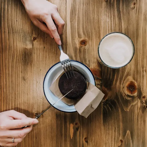 Kopp kaffe och chokladkaka på träbord. Händer med en gaffel och en kniv som skär en kaka. Med en röd bild. Vintage maträtt — Stockfoto
