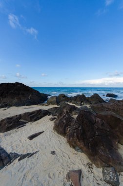 Doğal tropikal plaj, mavi gökyüzü ile kaya ve taş ön plan, parlak arka plan, ufuk yatay olarak.