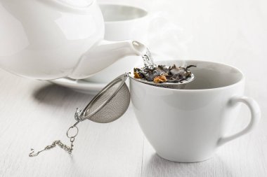 beyaz fincan içine çay demlik üzerinde sıcak su dökerek.
