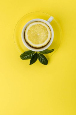çay limon dilimi ve çay yaprakları üzerinde sarı masa örtüsü.