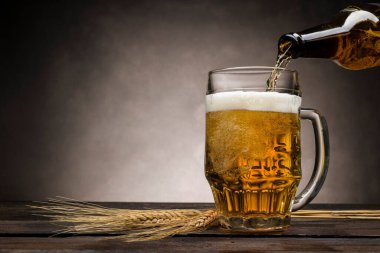 Sarı birayı cam pint 'e dökerek ahşap masaya, buğday kulaklarıyla