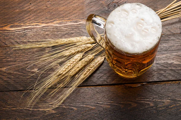 小麦の耳を持つ木製のテーブルの上に泡のビールパイントのトップビュー — ストック写真