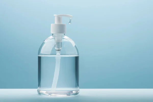 Dispenser of antibacterial gel with drop on blue background